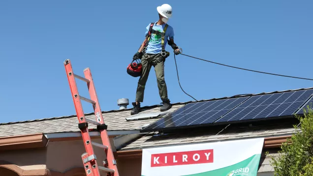 worker standing on roof installing solar panel